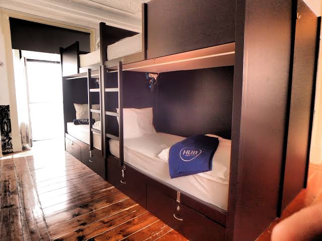 Compact hotel room with a bed against a plain wall and a shower cubicle beside it