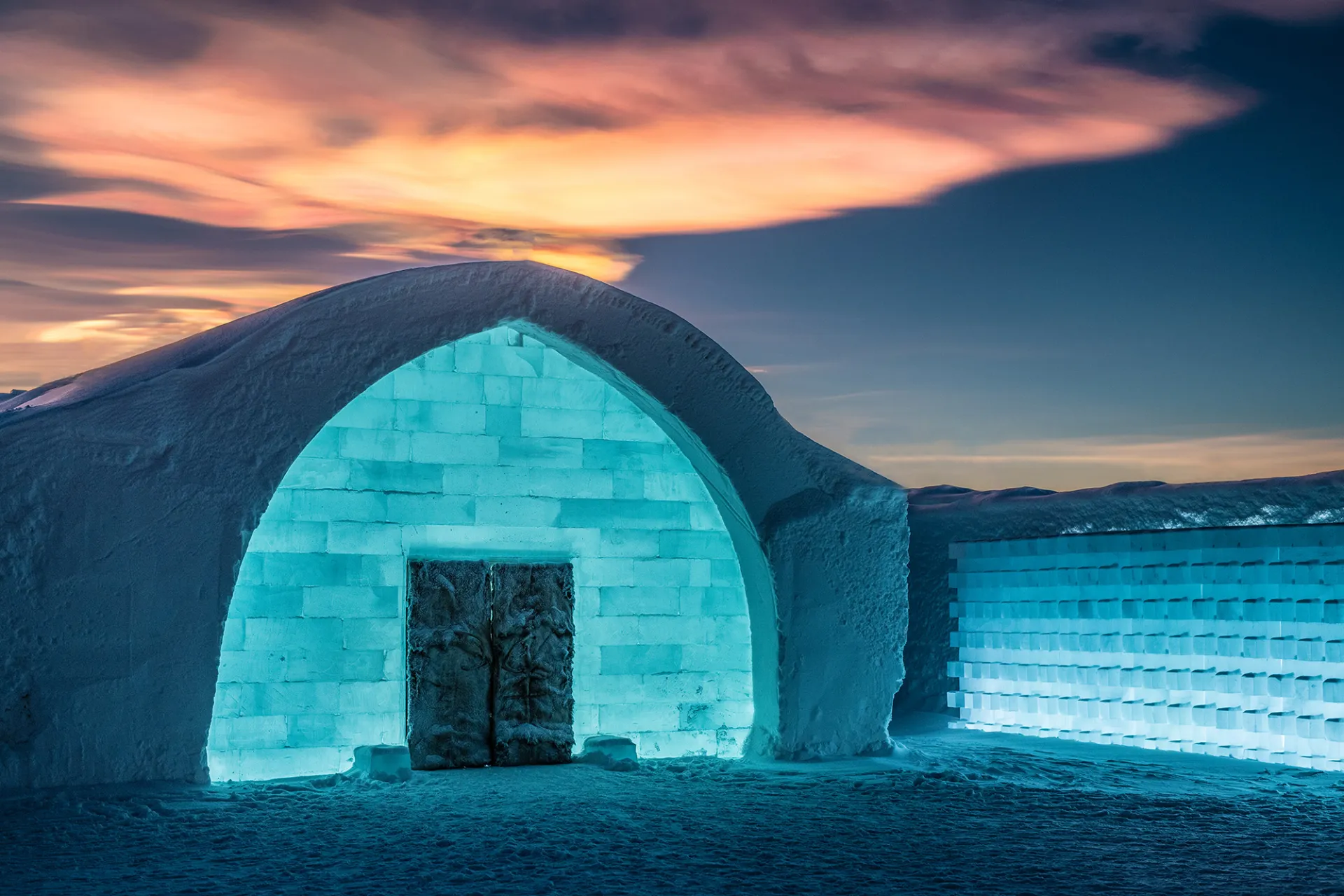Long snow-covered building beside a frozen river under low winter light